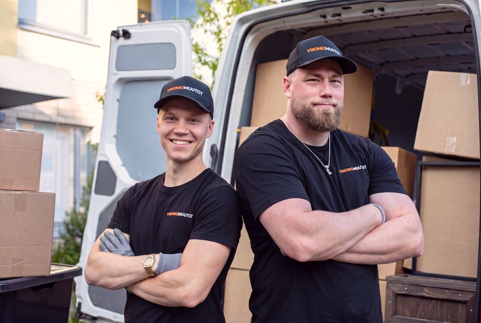 Kaksi Viikinkimuutot-muuttajaa hymyilee muuttoauton edessä